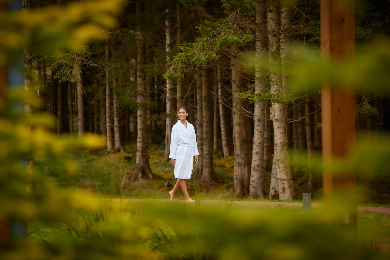 Lady dressed in a soft spa robe as she walks bare foot along a forest path.